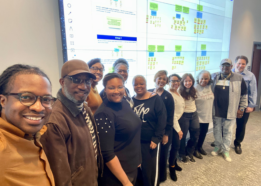 Group of individuals stand in front of a large projector screen and smile at the camera