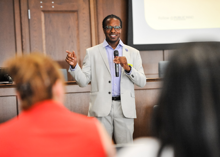 Public Innovation Fellow Terrance Smith in an auditorium holding a microphone points to his right